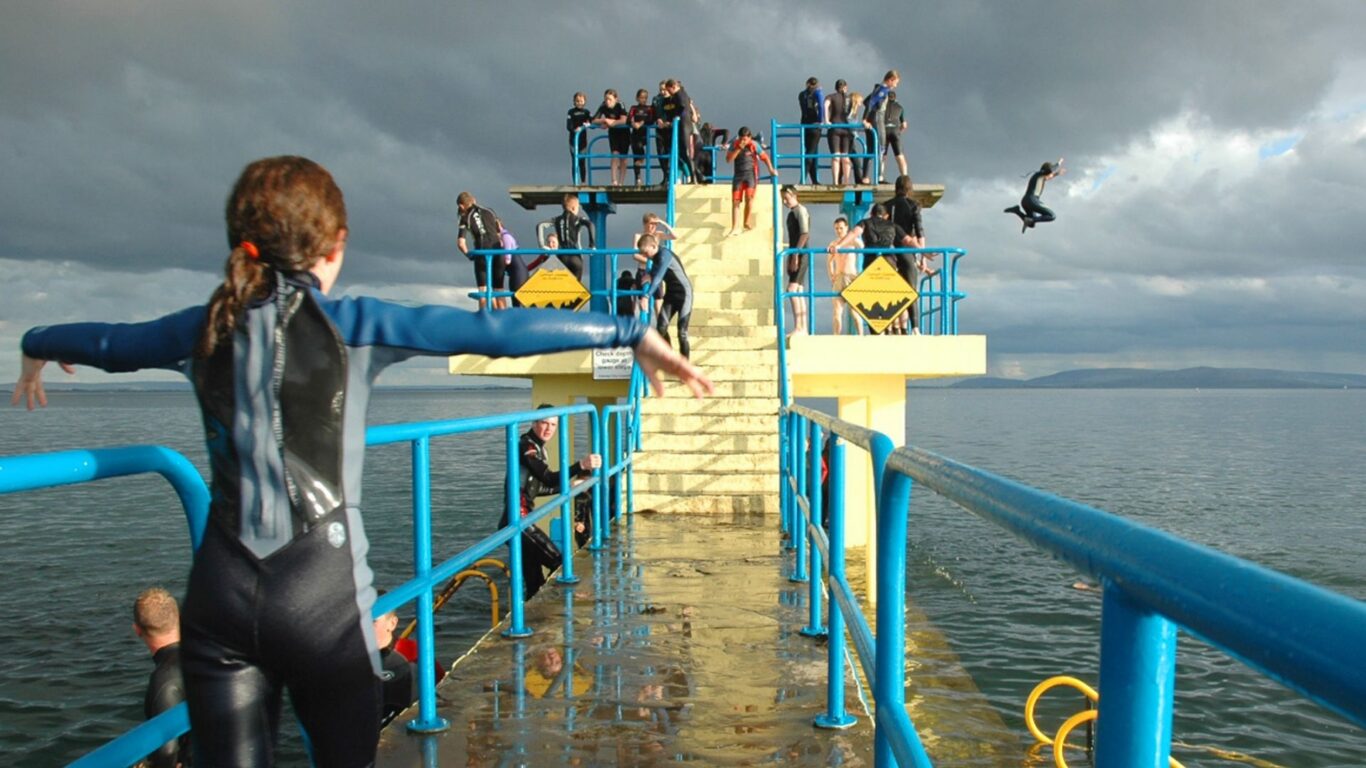 A girl in a wetsuit moving to the diving board in Salthill, Galway, Ireland. Oranmore Lodge Hotel is the best family hotel in Ireland with a swimming pool and is also close to all the best things to do in Galway with a family.